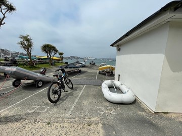 Photograph of the gable end of the public toilet building on the Strand, St Mary's, showing boat parking spaces currently occupied by boats and a bike.