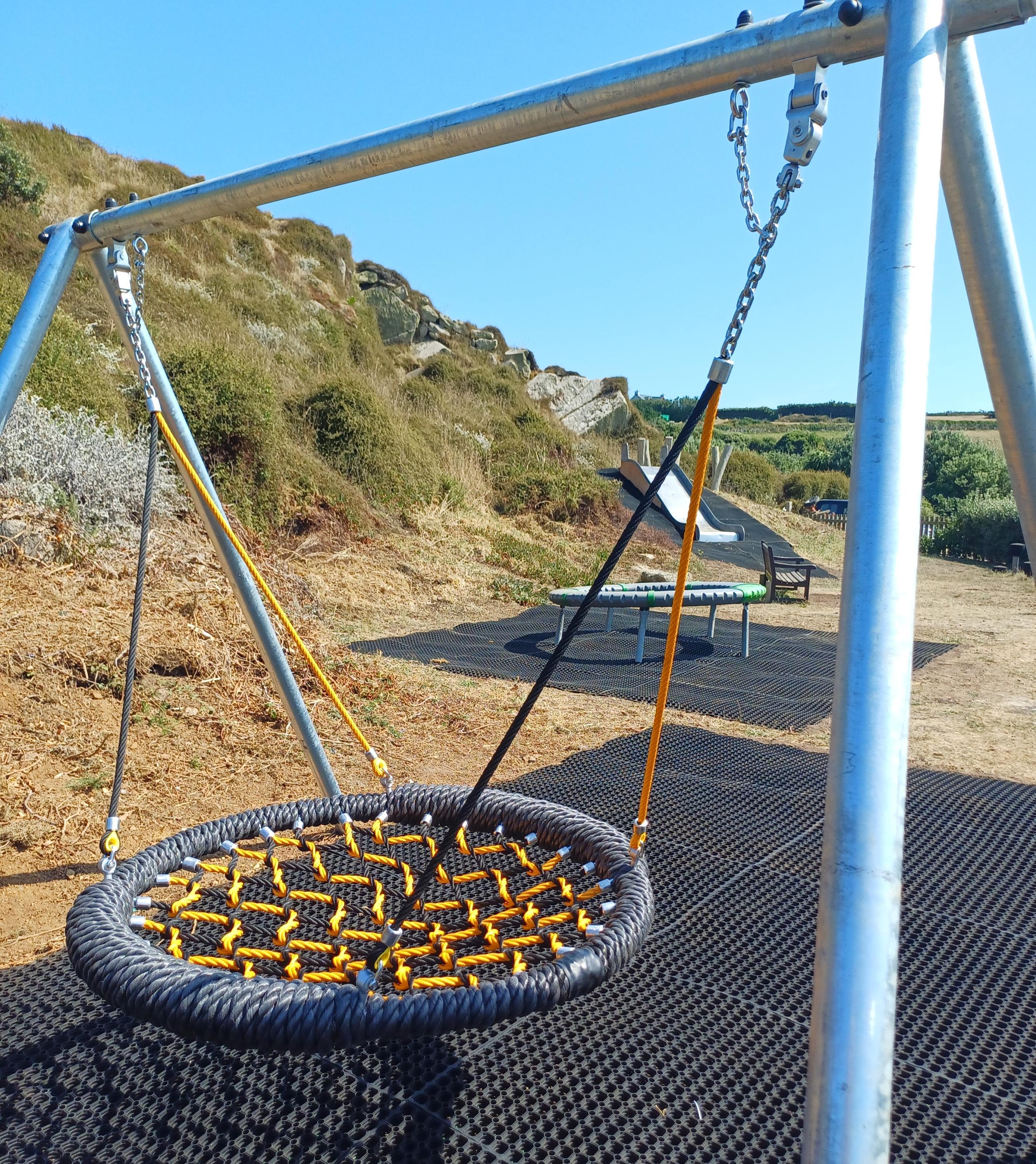 Close up image of the repaired play equipment at Porthcressa play park on St Mary's, including a swing, a roundabout and a slide.