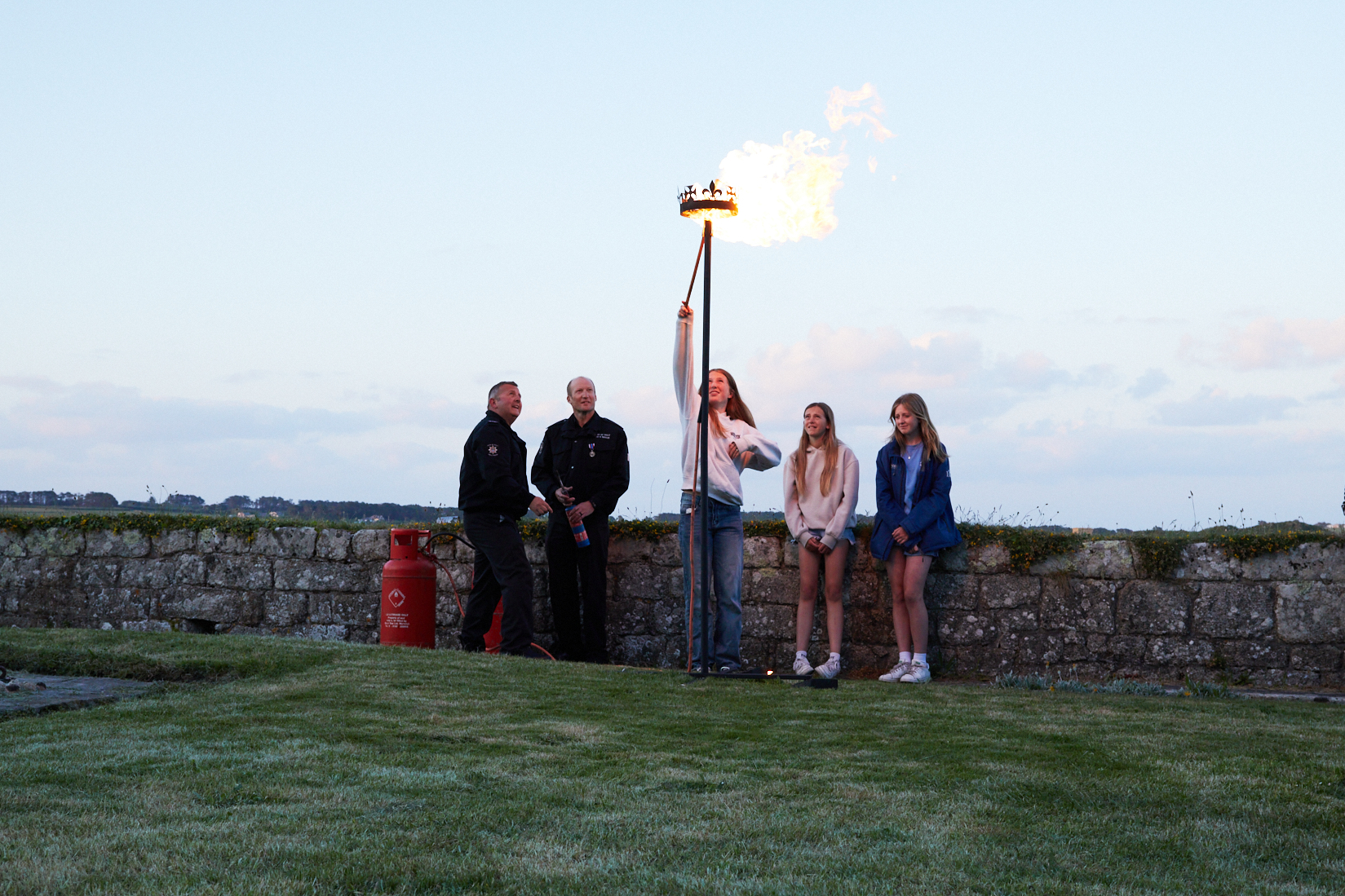 Photo of 3 year 9 students from Five Islands Academy lighting a beacon, assisted by members of the Isles of Scilly Fire and Rescue Service